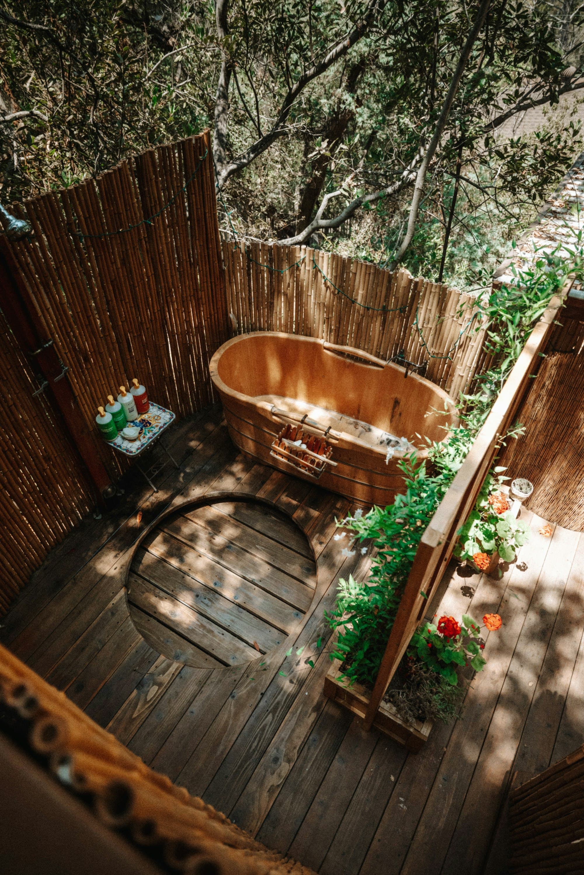 A wooden outdoor bathtub on a forest deck, dappled in afternoon light